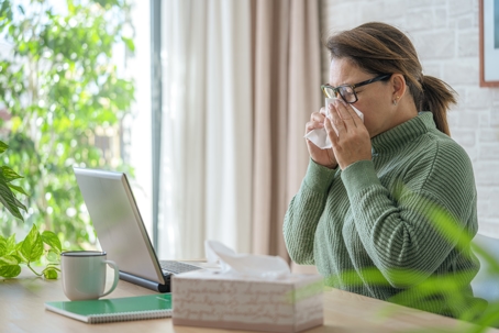 Woman working on laptop blowing her nose